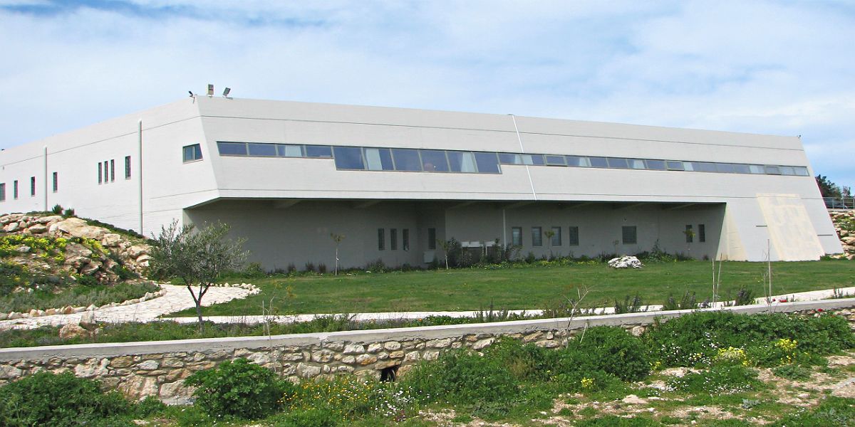 A modern building with a flat roof, large windows, and a stone retaining wall.