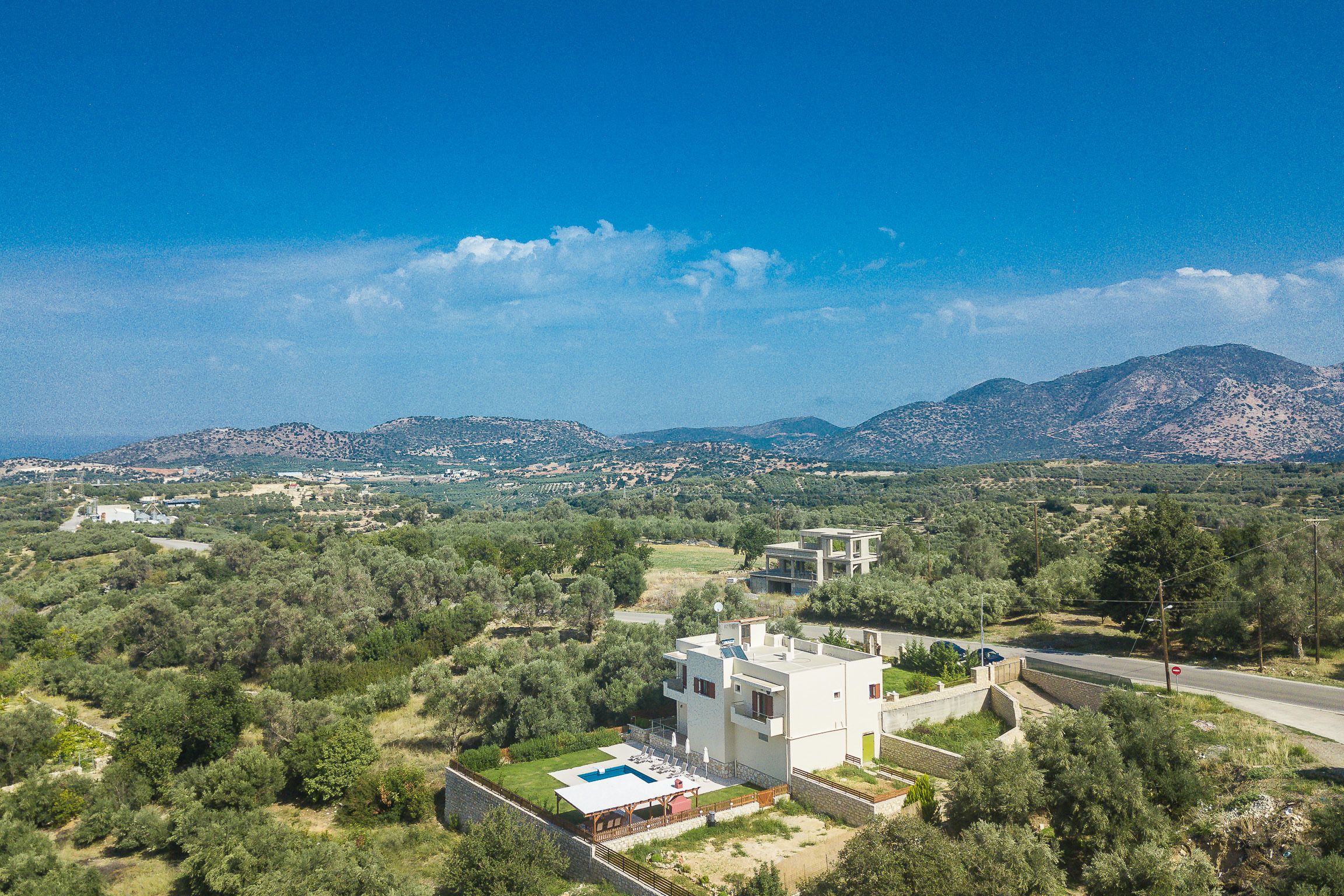 A modern villa with a swimming pool, surrounded by lush greenery and mountains in the background.