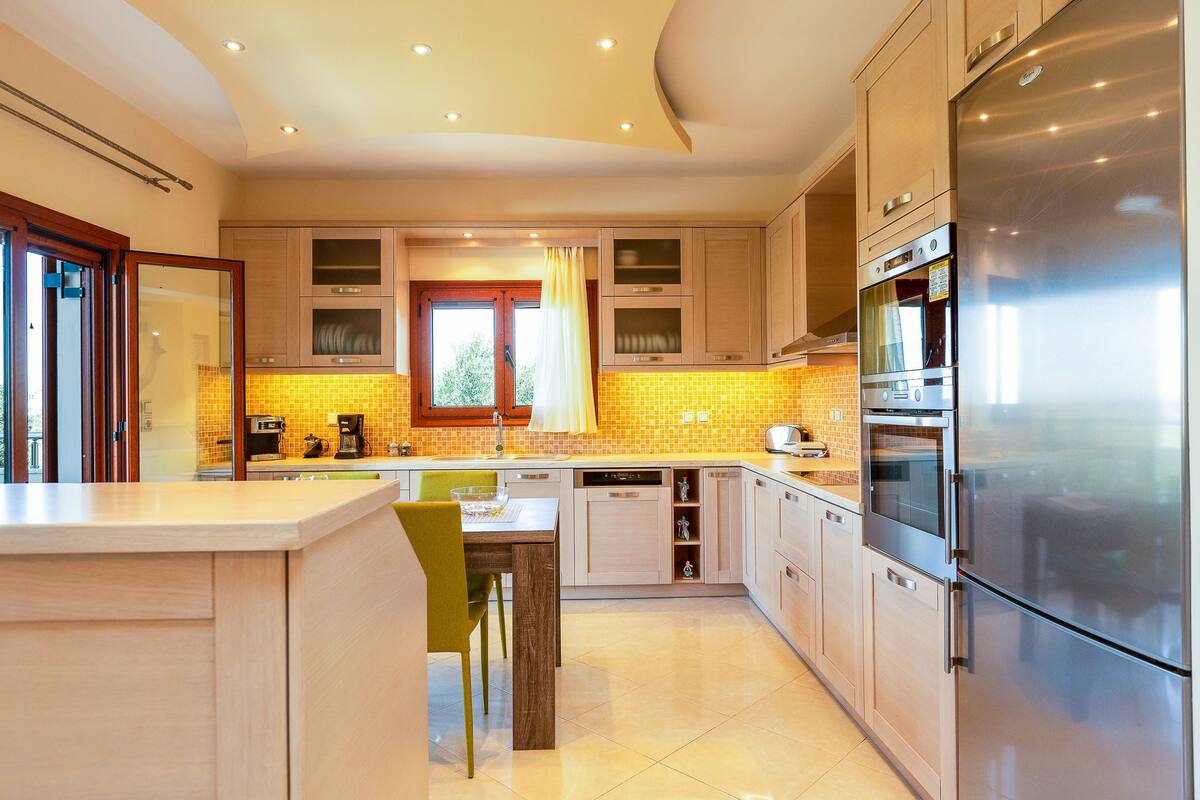 A modern kitchen with a large stainless steel refrigerator, built-in oven, and microwave. There is a dining area with a table and chairs.