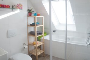 Bathroom features a bathtub, toilet, and storage shelf.