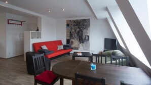 Una sala de estar moderna con un sofá rojo, una mesa de comedor con sillas, un mueble blanco y un cuadro abstracto grande en la pared.