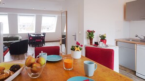 Una cocina moderna con comedor, que incluye una mesa de madera adornada con frutas, una taza de café y un jarrón con flores.