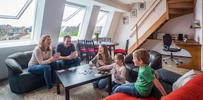 Una familia jugando a las cartas en una sala de estar moderna con tragaluces, una escalera y vistas al vecindario.