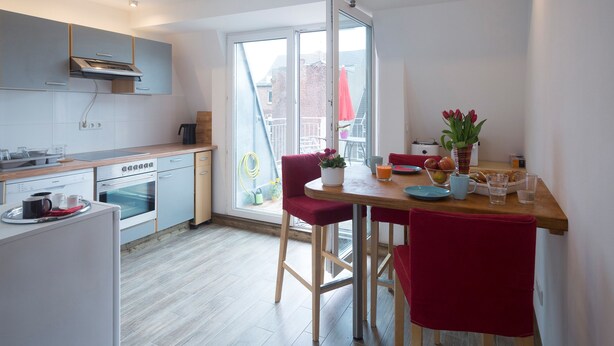Una cocina moderna con comedor, que cuenta con un amplio ventanal, piso de madera y sillas rojas.