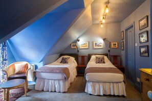 Een slaapkamer met twee bedden, een stoel, een tafeltje en een dressoir.
