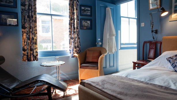 A hotel room with a bed, a chair, a small table, and a window with curtains. - Hill View House (Dartmouth)