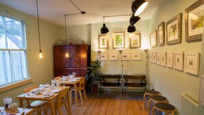 A dining area with wooden tables and chairs, a wooden cabinet, and framed pictures on the wall. - Hill View House (Dartmouth)