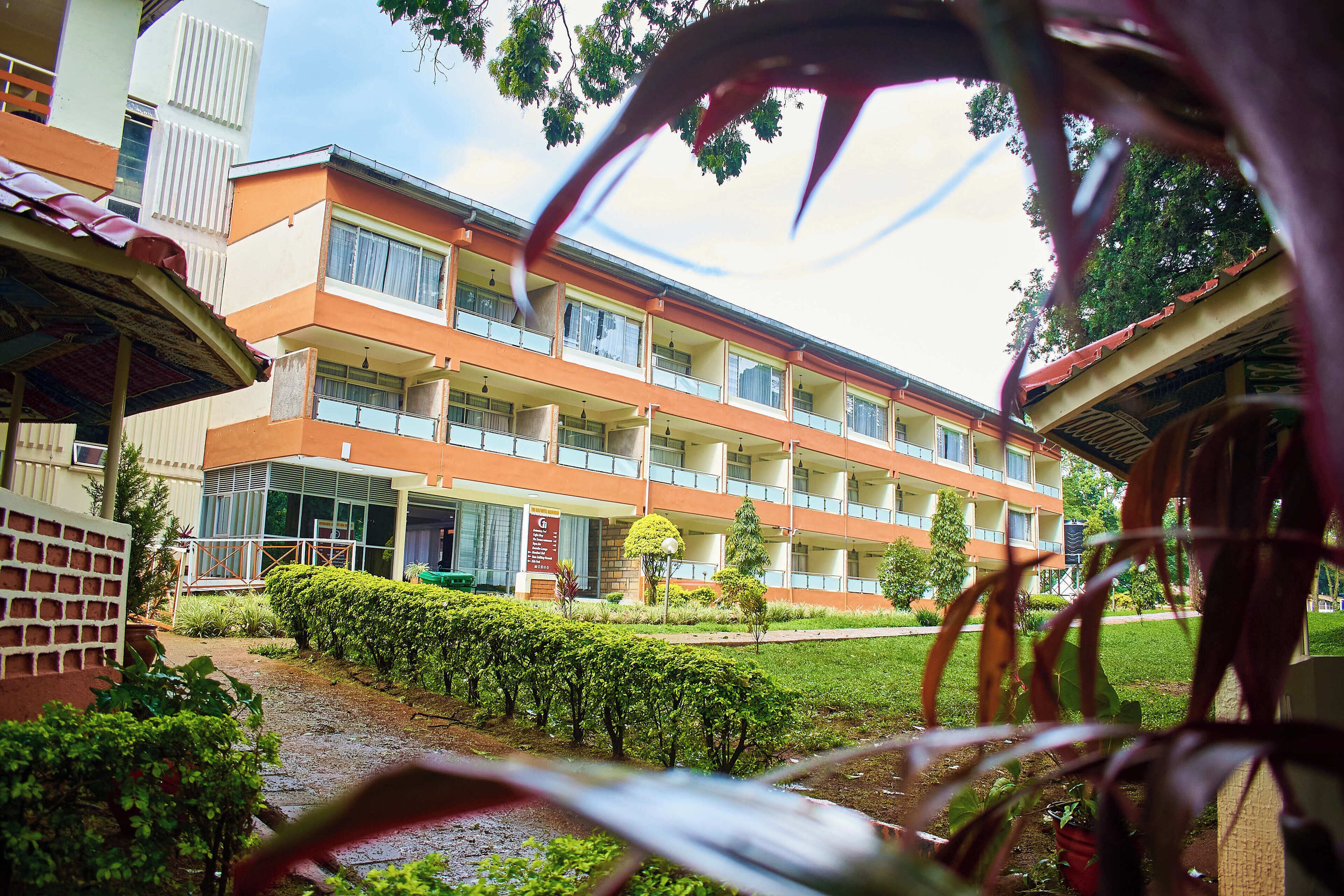 A multi-story building with balconies, a garden area, and a pathway leading to the entrance.