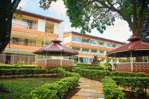 A hotel with a courtyard featuring a pathway, neatly trimmed bushes, and two red-roofed gazebos.