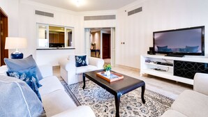 A modern living room with a flat-screen TV, white sofas, a coffee table, and a patterned rug. - Fairmont North Luxury 2 BR Apt Palm (Dubai)