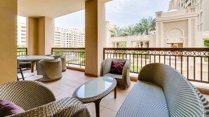 A balcony with wicker furniture, a glass table, and a view of a building with arches and a balcony railing. - Fairmont North Luxury 2 BR Apt Palm (Dubai)