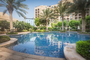 A swimming pool with tiled edges, surrounded by palm trees and greenery, with a multi-story building in the background. - Fairmont North Luxury 2 BR Apt Palm (Dubai)