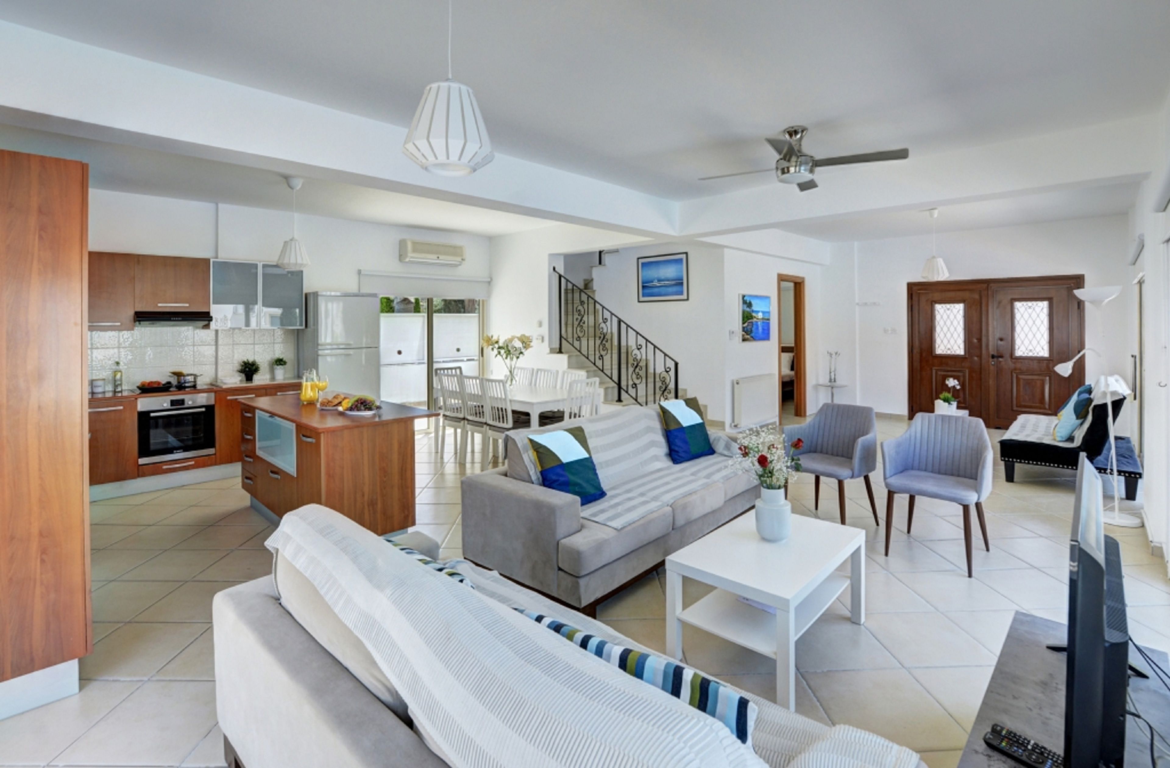 A spacious living area with a sofa, coffee table, and a TV. A kitchen with modern appliances and a dining area with chairs and a table are visible.