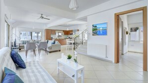 Un vaste espace de vie comprenant un canapé, une table à manger et des chaises, une cuisine à l’arrière-plan et un escalier menant à l’étage supérieur.