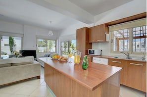 A modern kitchen with wooden cabinets, a central island, and a dining area with a sofa. - Blue Sea Villa (Paralimni)