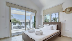Une chambre avec un grand lit, un balcon avec vue et un chapeau accroché au mur.