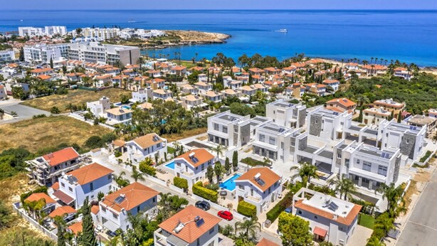 Une zone résidentielle côtière avec des maisons modernes, une mer d’un bleu limpide et une petite île visible au loin.