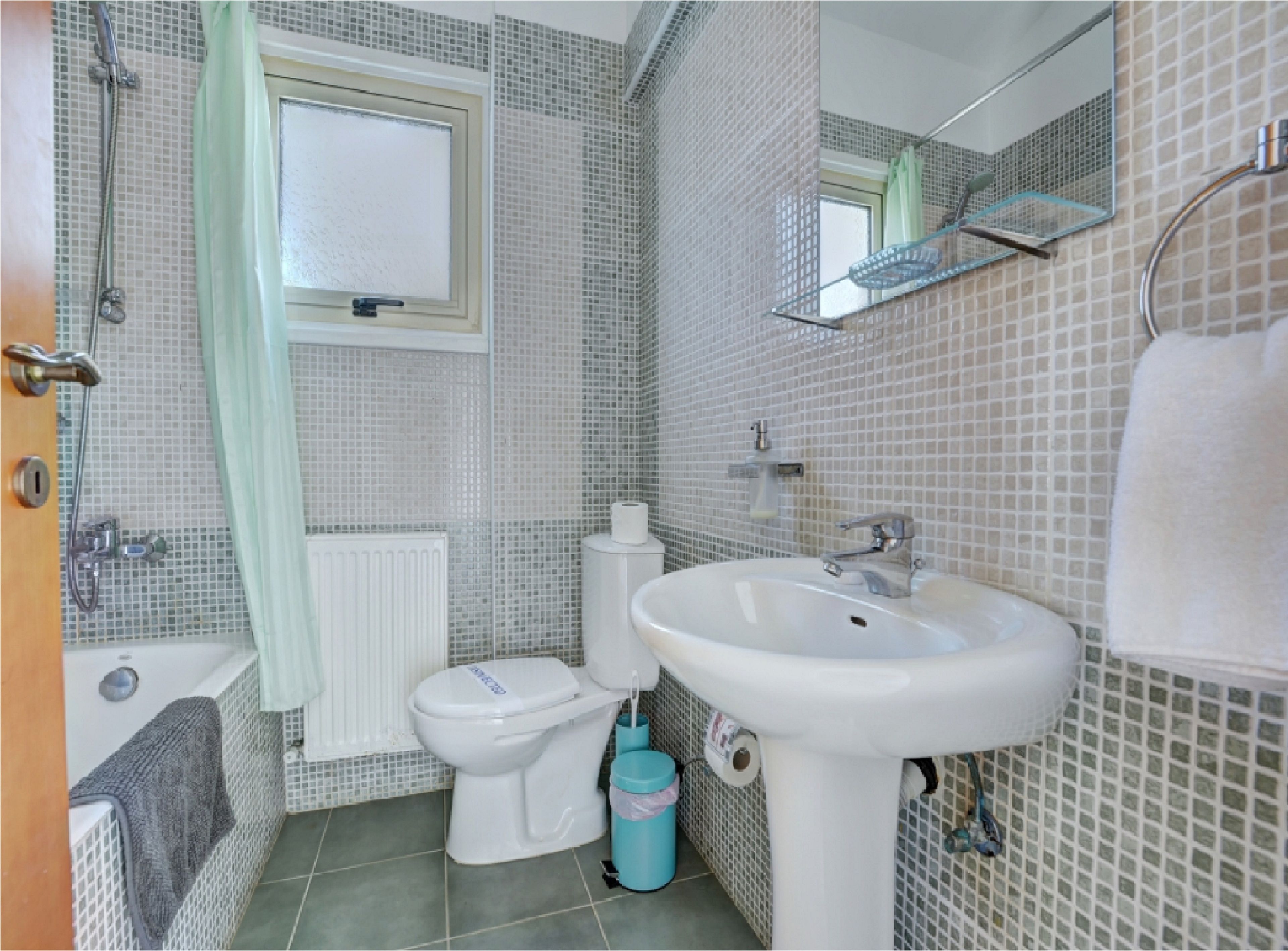 A bathroom with a toilet, sink, shower, and a window.