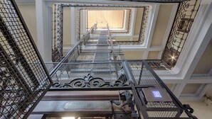 Interior de varios niveles con barandillas de metal, una escalera central y un cartel con un símbolo.