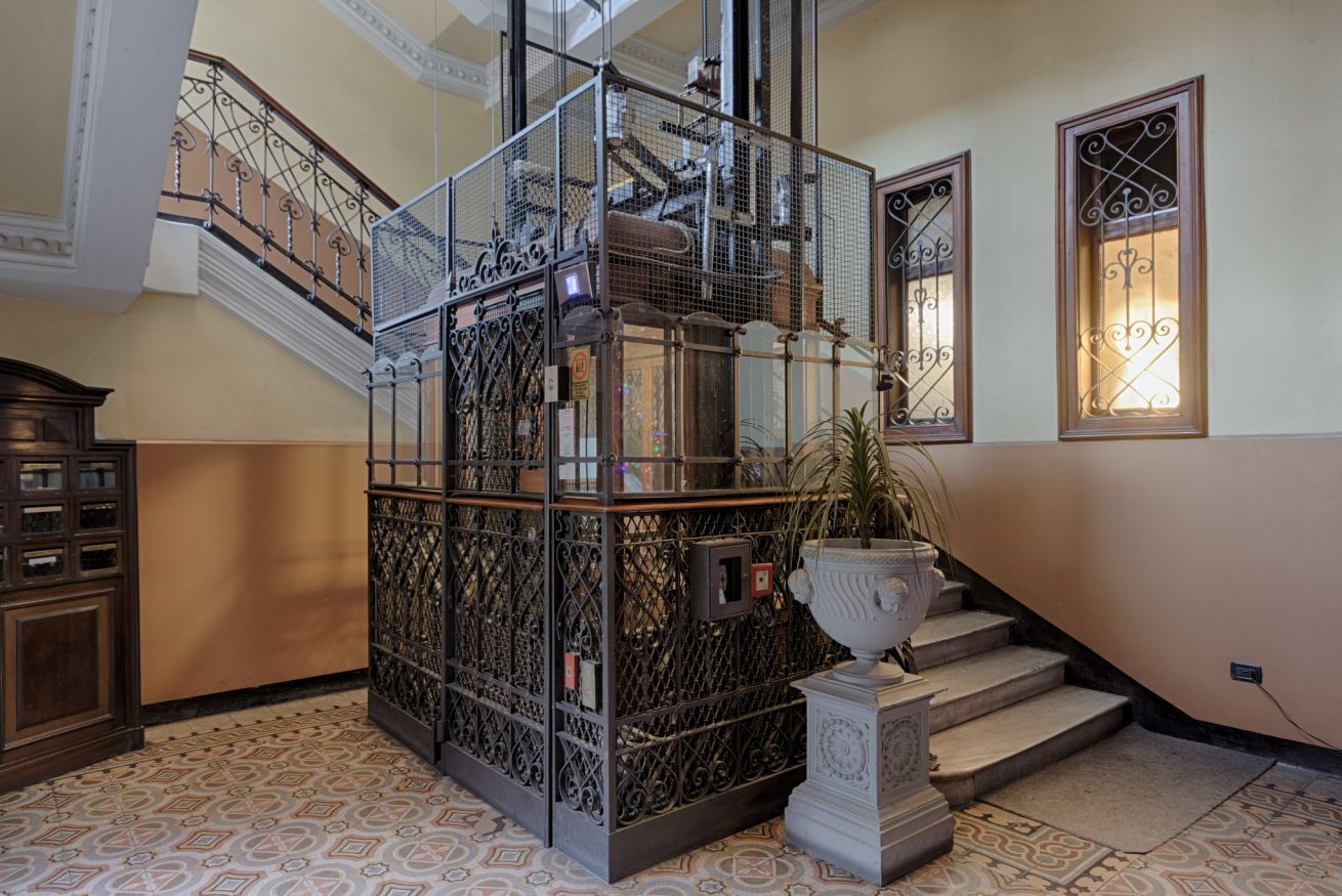 Una escalera con barandillas metálicas ornamentales, una planta en maceta y una urna decorativa.
