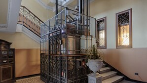 Una escalera con barandillas metálicas ornamentales, una planta en maceta y una urna decorativa.