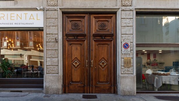 Una puerta doble de madera tradicional con tallas intrincadas, un letrero de restaurante japonés y una señal de no estacionamiento.
