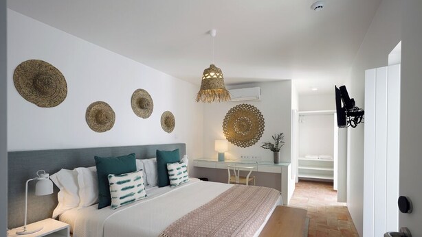 A bedroom with a bed, bedside table, lamp, and decorative wall hangings. - Alte Tradition Guest House (Loulé)
