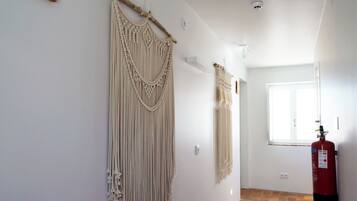 Un pasillo con tapices de macramé, un extintor y una ventana con luz natural.