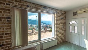 A room with a large window offering a city view, a radiator, and a door with glass panels. - Contessa Apartments (Budva)