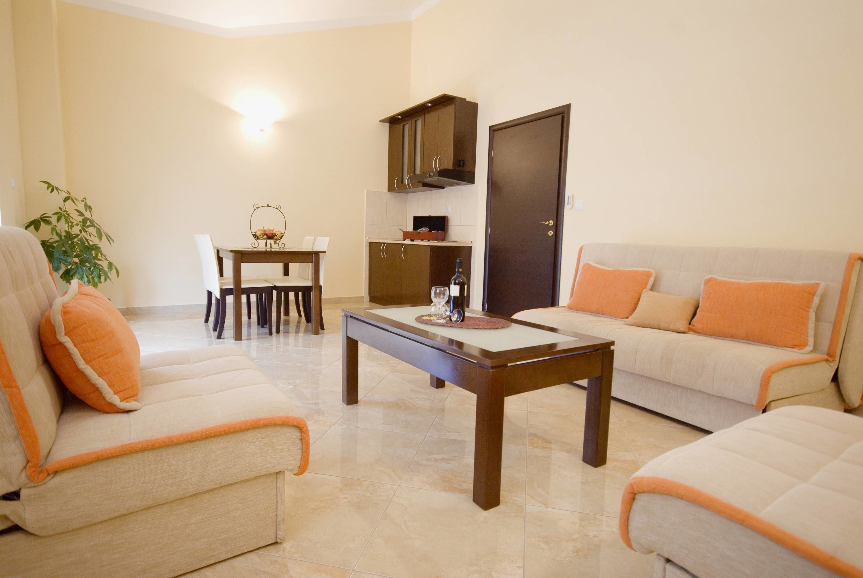 A living room with a sofa, a coffee table, a dining table with chairs, a kitchen area with cabinets, and a door.
