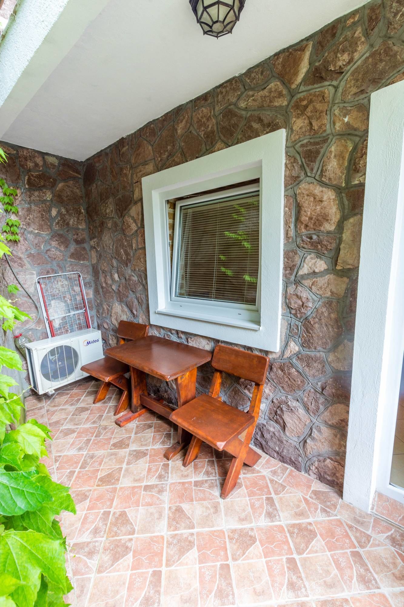 Una pared de piedra con una ventana, una mesa con bancos y un equipo de aire acondicionado.