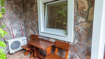 Una pared de piedra con una ventana, una mesa con bancos y un equipo de aire acondicionado.