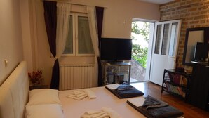A bedroom with a bed, a TV, a radiator, and a bookshelf. - Contessa Apartments (Budva)