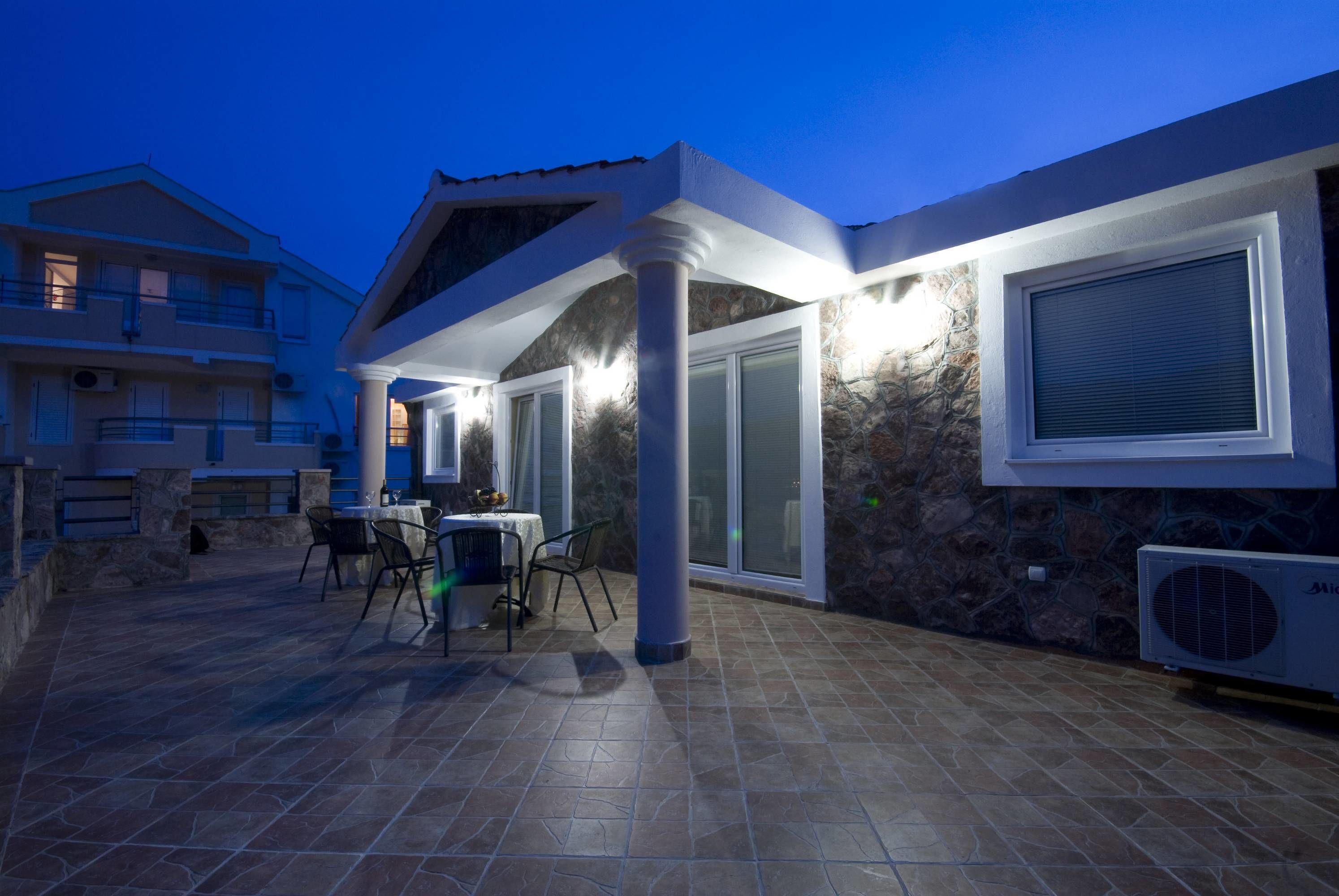 An outdoor patio area with a table and chairs, a stone wall, and a covered seating area with a glass door.