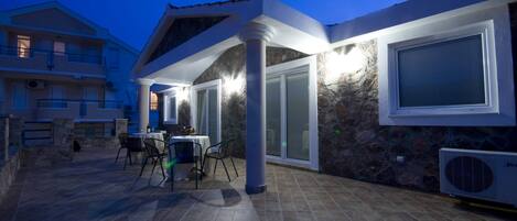 An outdoor patio area with a table and chairs, a stone wall, and a covered seating area with a glass door.