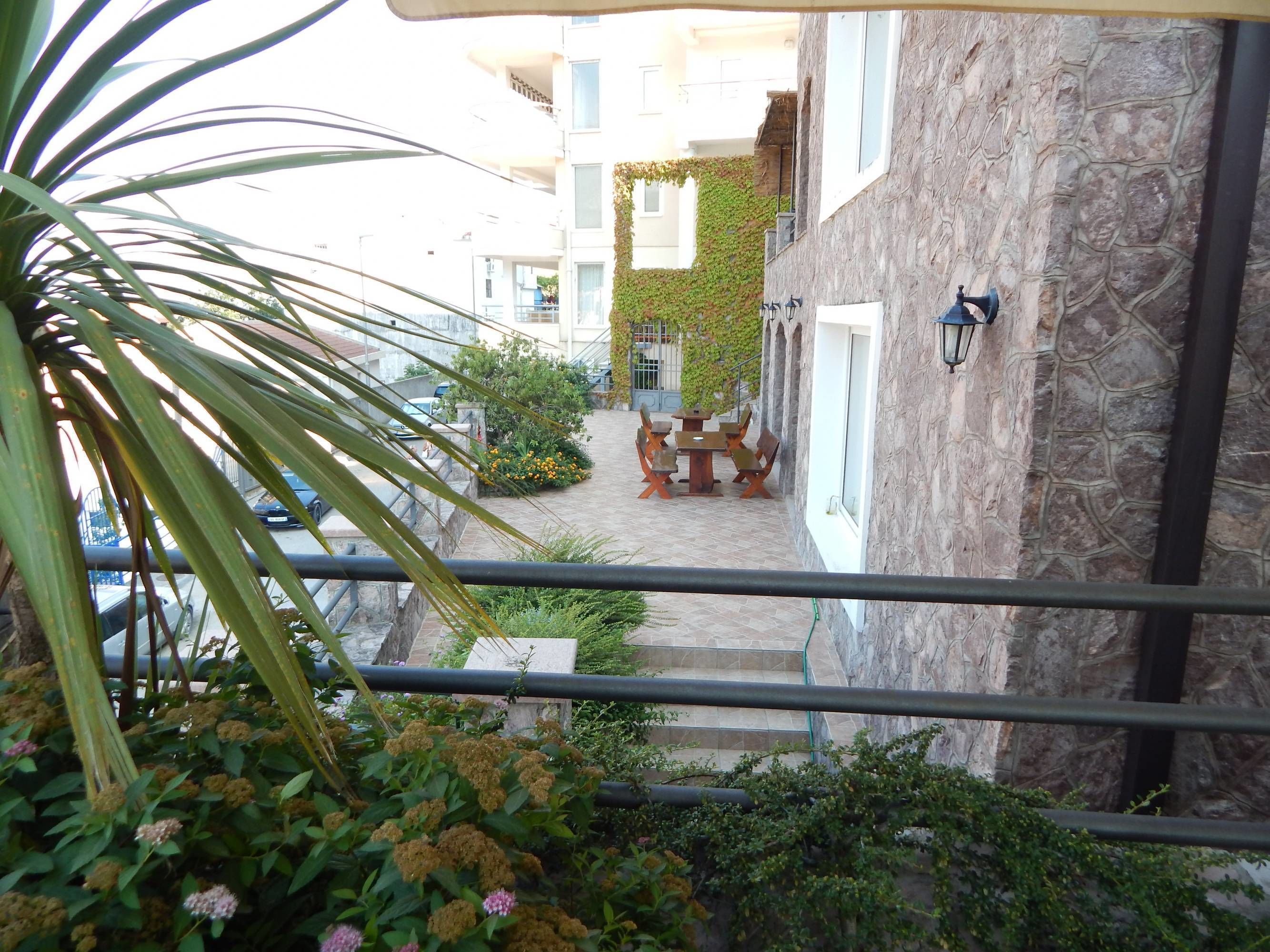 Un patio con un muro de piedra, una mesa y sillas de madera, y una pequeña zona ajardinada con plantas y flores.