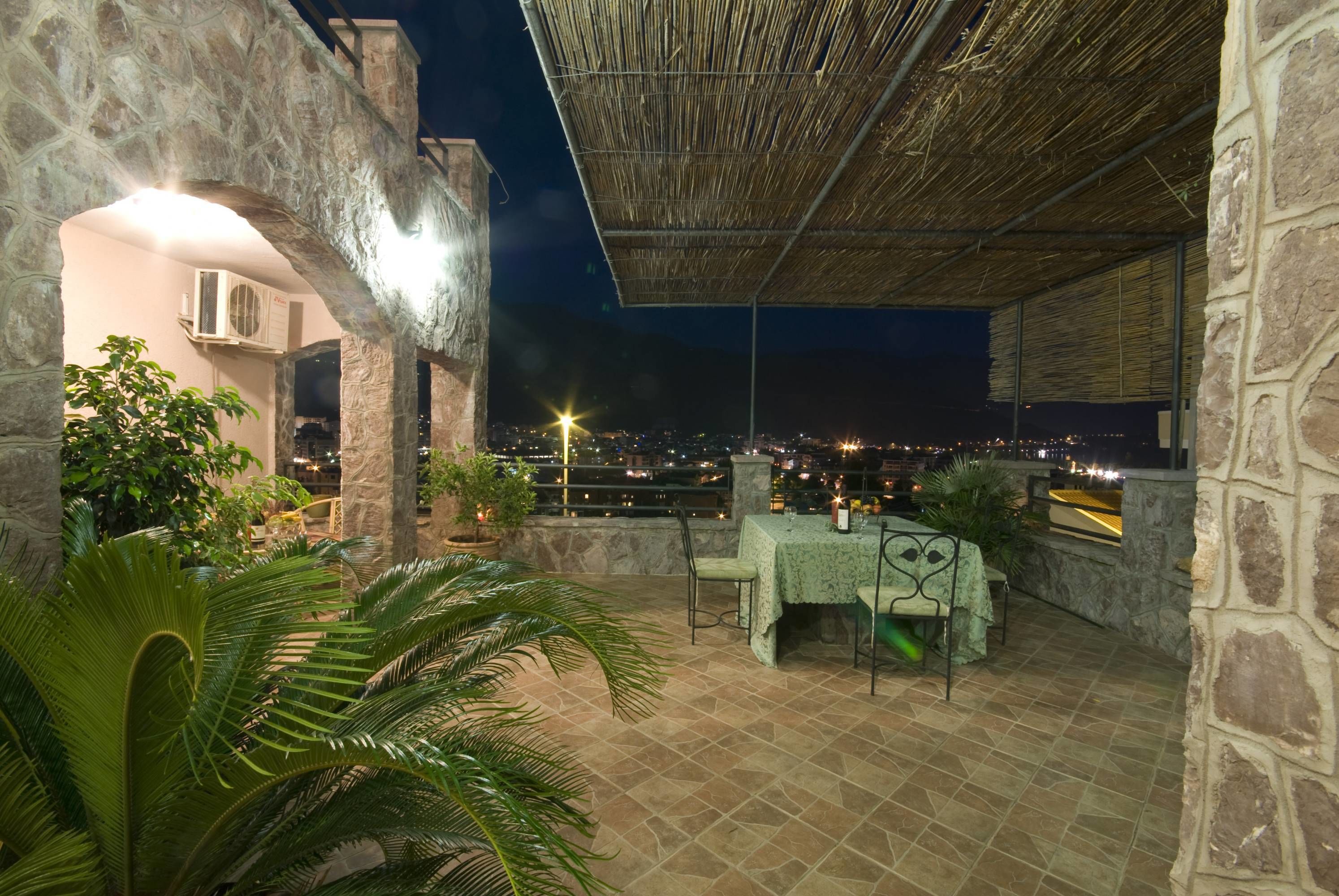 Patio esterno con pareti in pietra, un tavolo con sedie e vista sulla città illuminata di notte.