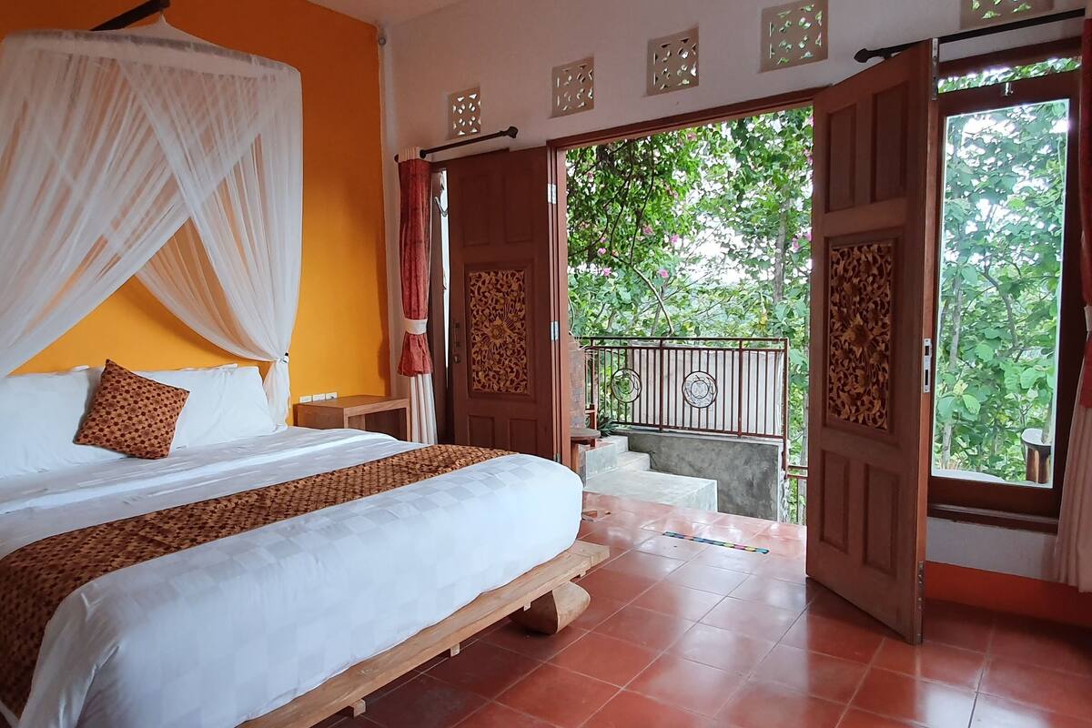 Un dormitorio con cama, mesita de noche, cortinas y vistas al exterior.
