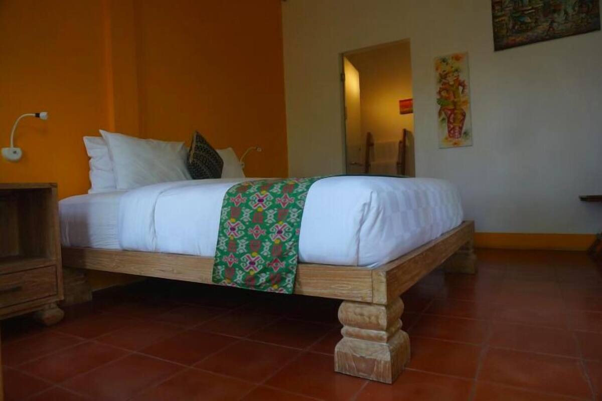 Un dormitorio con estructura de cama de madera, ropa de cama blanca y una manta de color verde con estampado.