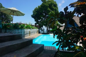A swimming pool with steps leading up to it, surrounded by lush greenery and a clear blue sky.