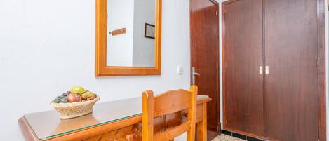 Ein Holztisch mit Glasplatte und einem Korbfruchtregal, ein Holzstuhl, ein Spiegel und zwei Holztüren.