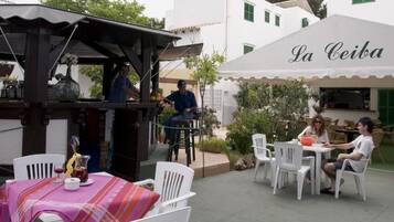 Ein Außenbereich mit Tischen und Stühlen, eine Bar und ein Gebäude mit der Aufschrift 'La Ceiba'.