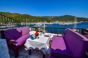 A terrace with purple seating, a table set for two, and a view of a marina with boats and hills in the background. - Mets Boutique Hotel (Marmaris)