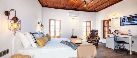 A room with a wooden ceiling, a bed with pillows, a desk with a chair, and a television on the wall.