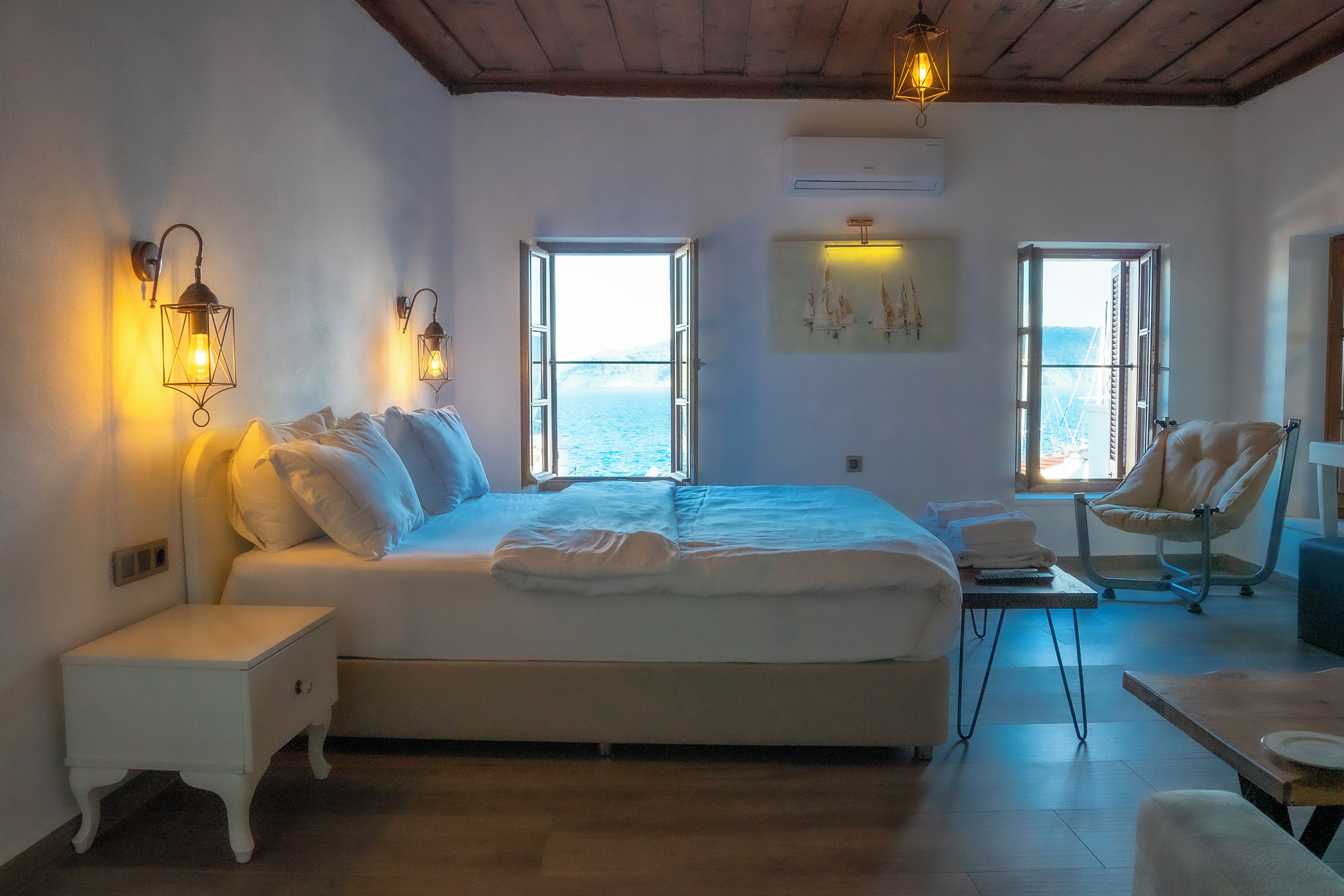 Une chambre à coucher avec un lit, deux lampes de chevet, une chaise, une table et un tableau accroché au mur.