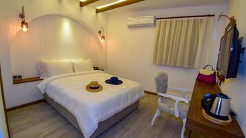 Quarto bem arrumado com cama, abajures, uma cadeira, escrivaninha com chaleira e ar condicionado.