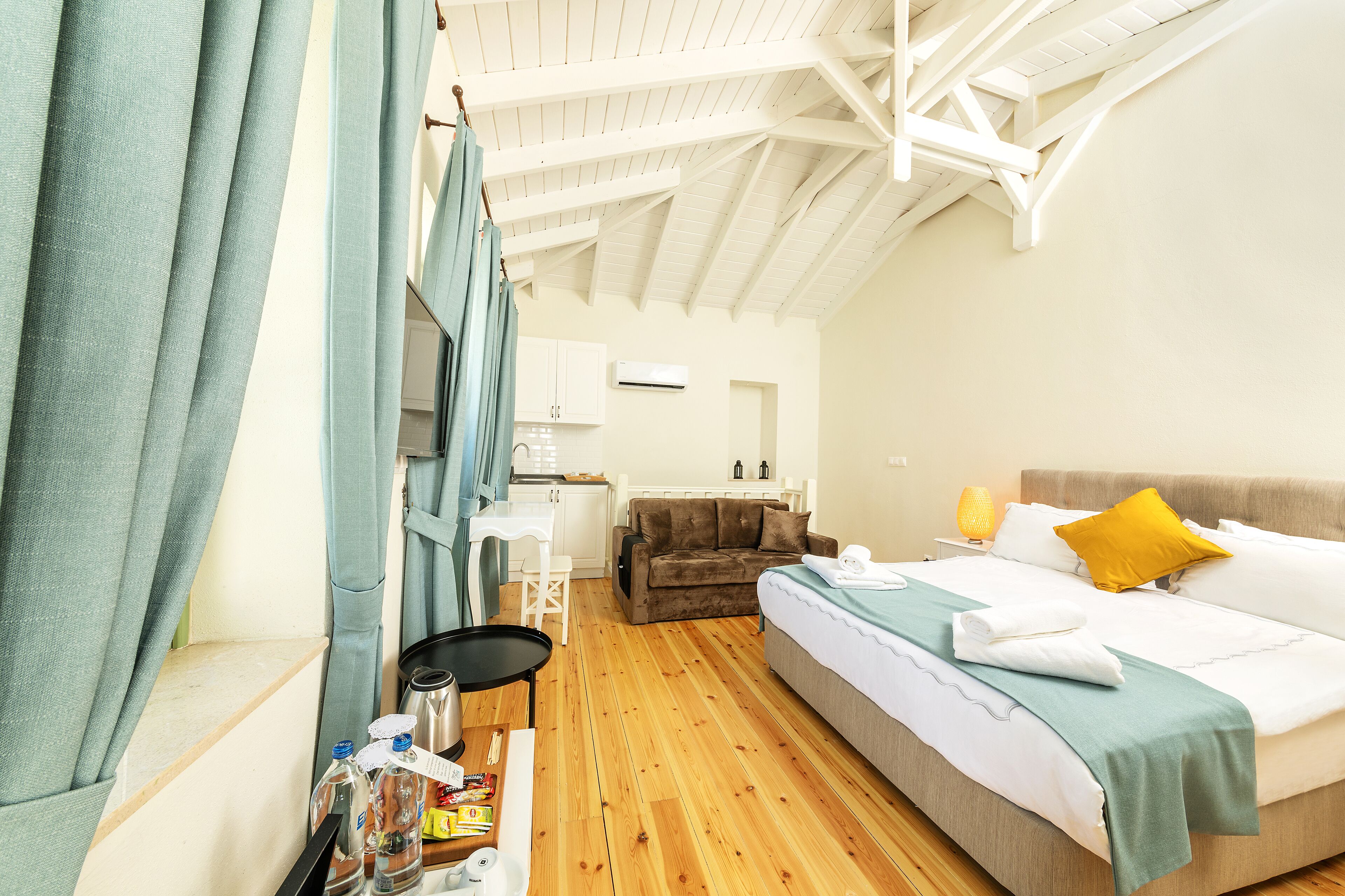 Una habitación con cama, sofá, una mesa con lámpara y una kitchenette al fondo.
