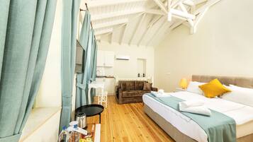 Una habitación con cama, sofá, una mesa con lámpara y una kitchenette al fondo.