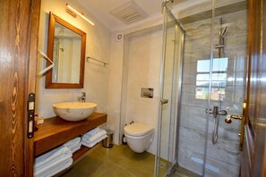 A bathroom with a wooden vanity, a large mirror, a white sink, a toilet, and a glass-enclosed shower. - Mets Boutique Hotel (Marmaris)