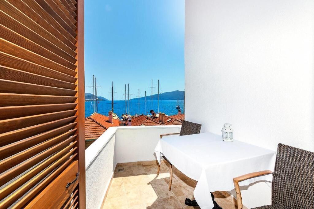 A balcony with a table and chairs, a view of the sea, and a wooden slatted wall.